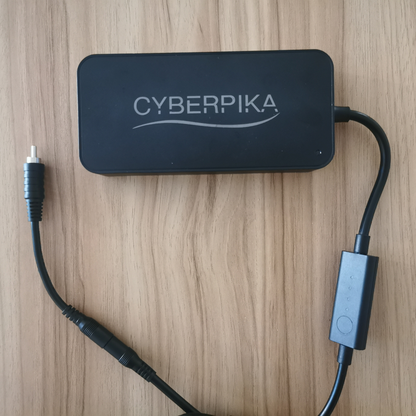 A black Cyberpika electronic adapter or power supply with attached cables, placed on a light wood-grained surface.